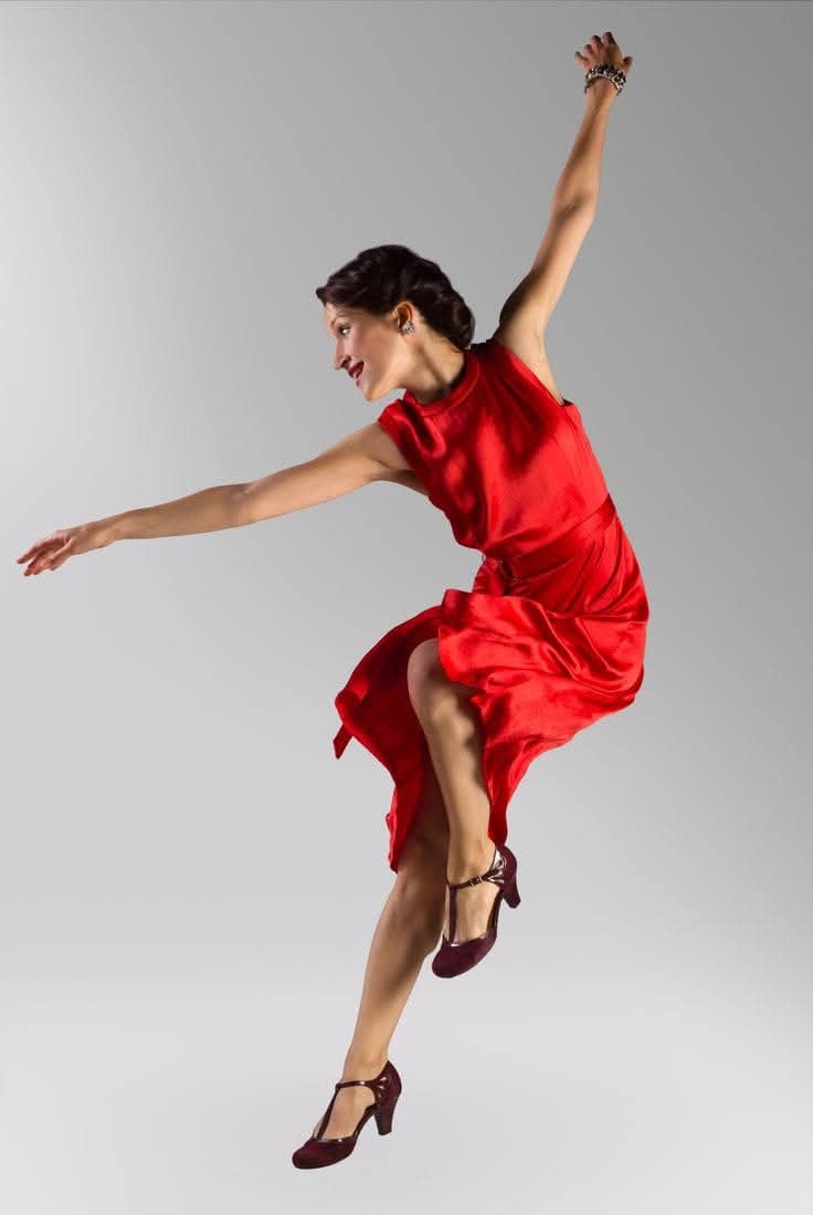Ballerina in abito rosso che danza individualmente con le braccia aperte