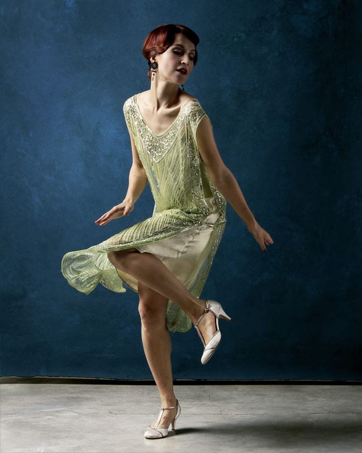 Ballerina in abito vintage verde che esegue un passo individuale su sfondo blu